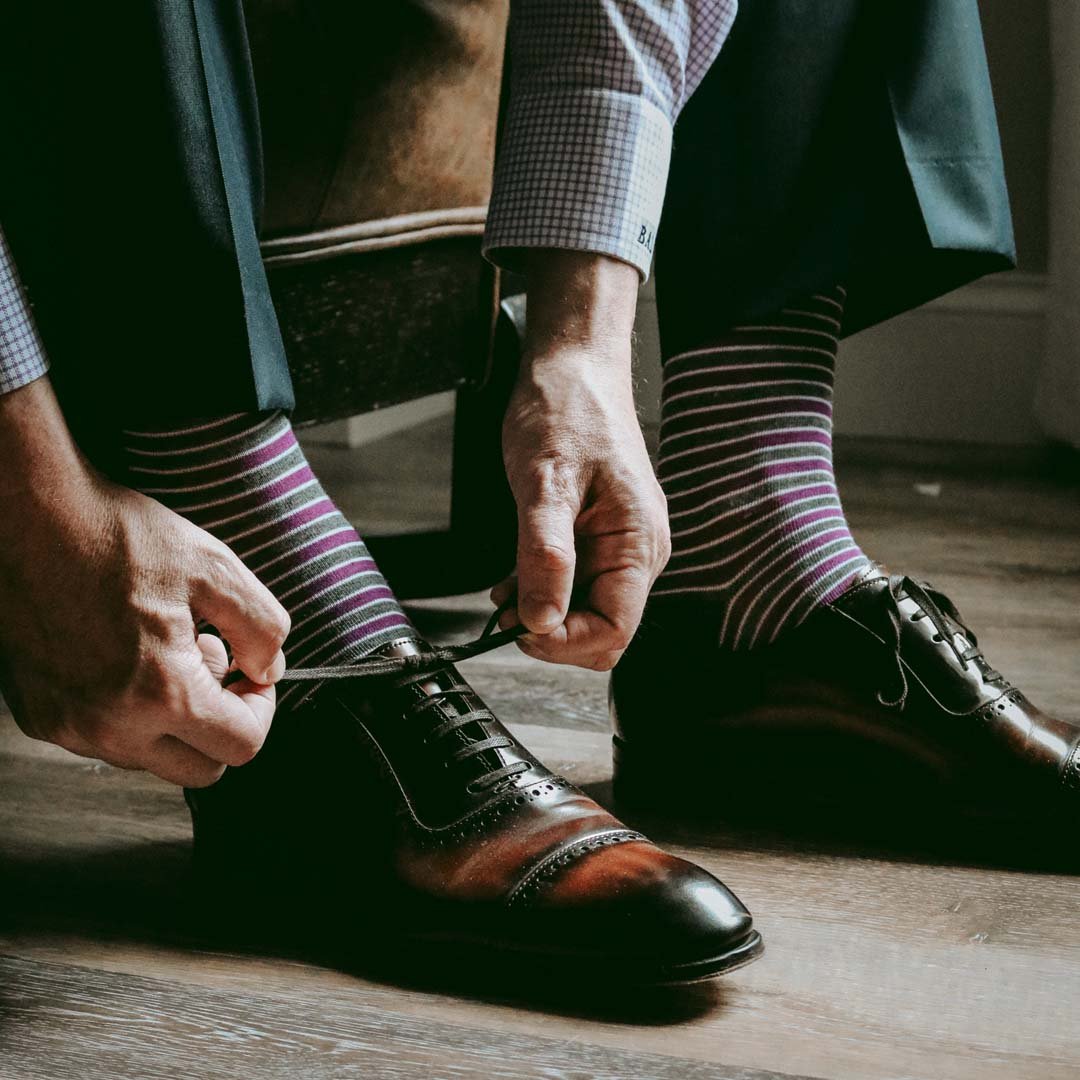 Man sitting wearing purple, grey, and white striped dress socks and brown dress shoes
