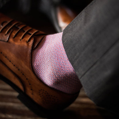 A close up shot of a man wearing tan dress shoes, salmon colored socks, and grey trousers