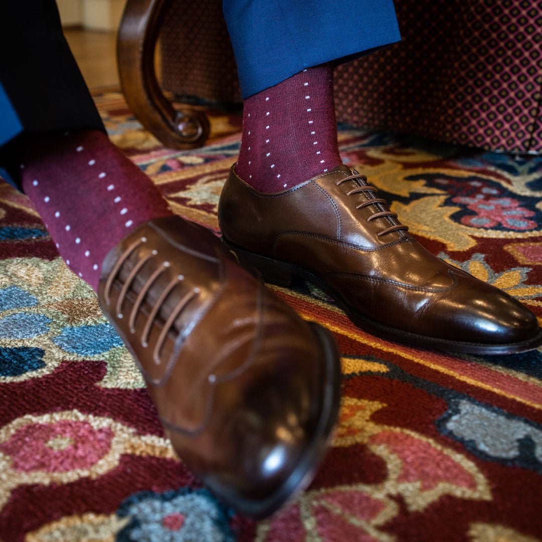 Man wearing Deep red sock with light blue pin dots, brown shoes, and blue trousers