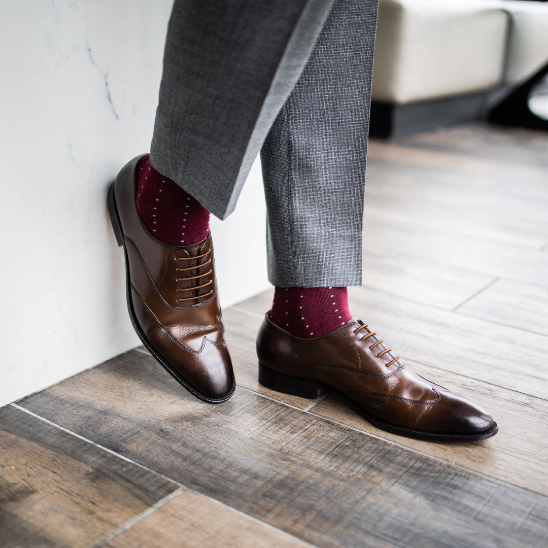 Man wearing Deep red sock with light blue pin dots, brown shoes, and grey slacks