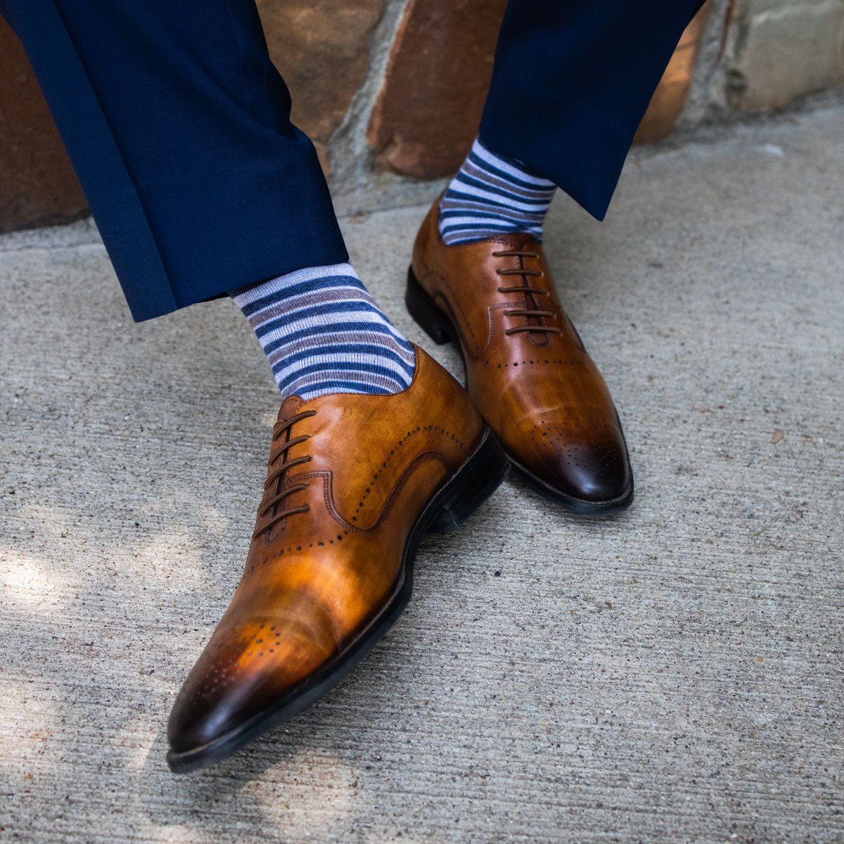 a man wearing grey, blue, and white striped men's dress socks with brown shoes and blue slacks