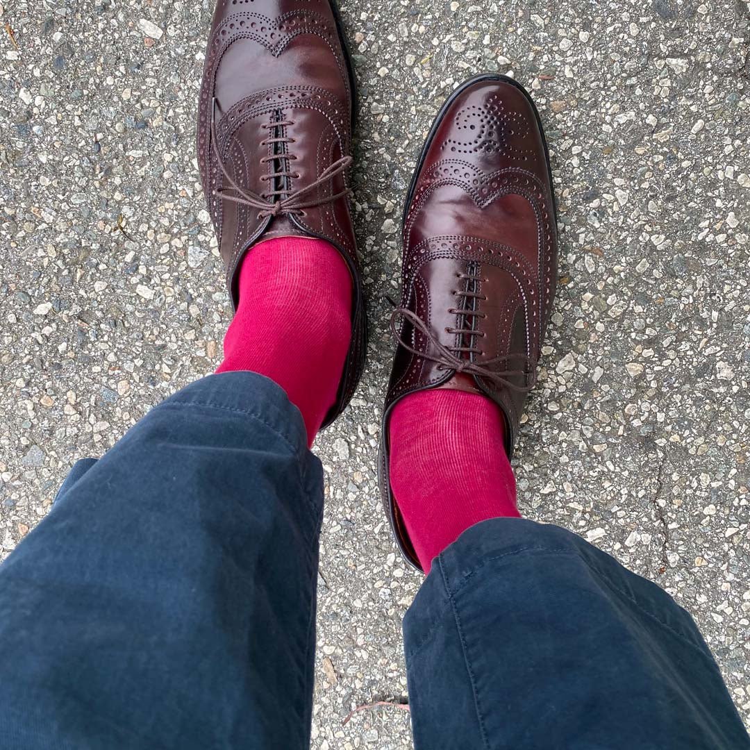 Man standing wearing ruby men's dress socks and brown shoes.