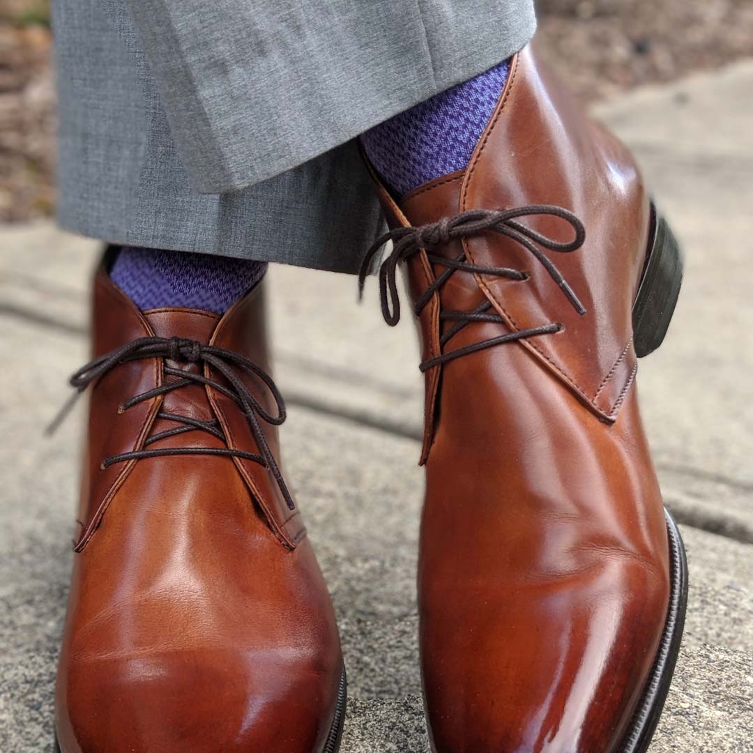 Man standing with feet crossed wearing purple socks and brown shoes