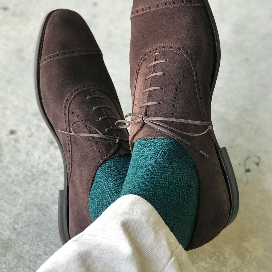 Man sitting with legs crossed wearing hunter green socks and dress shoes
