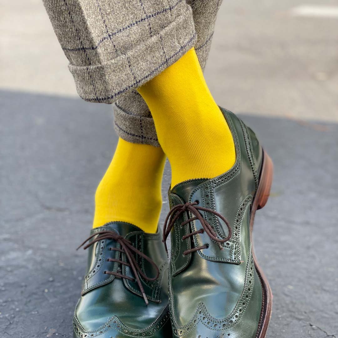 Man standing with feet crossed wearing canary yellow men's dress socks and shoes.