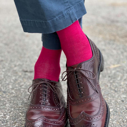Man standing with feet crossed wearing ruby men's dress socks and brown shoes.