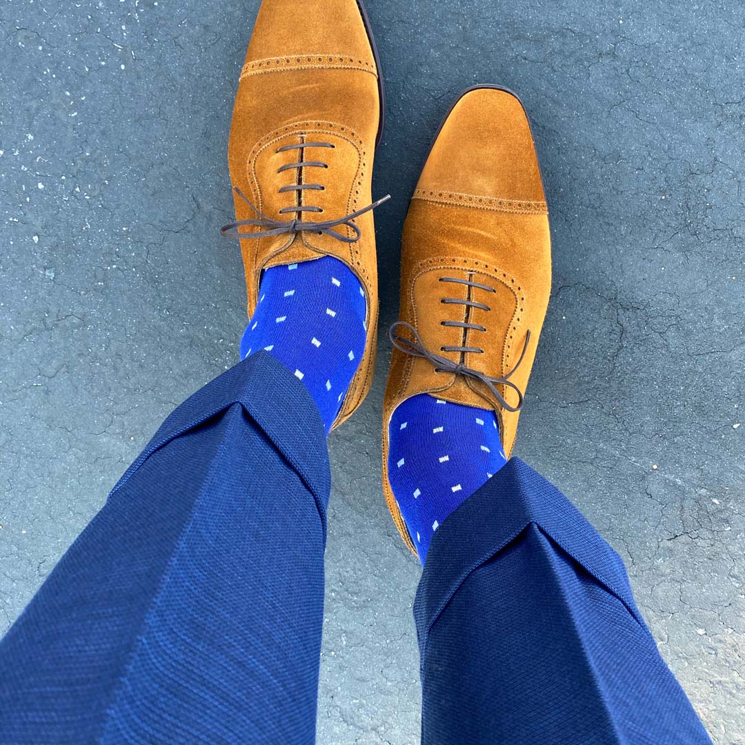 Man standing wearing sapphire blue, sand and white socks with brown shoes