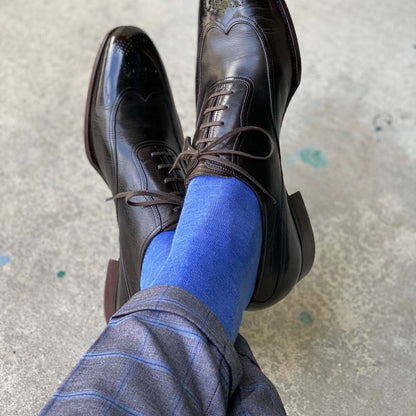Man sitting down with legs crossed wearing steel blue men's dress socks and black shoes.