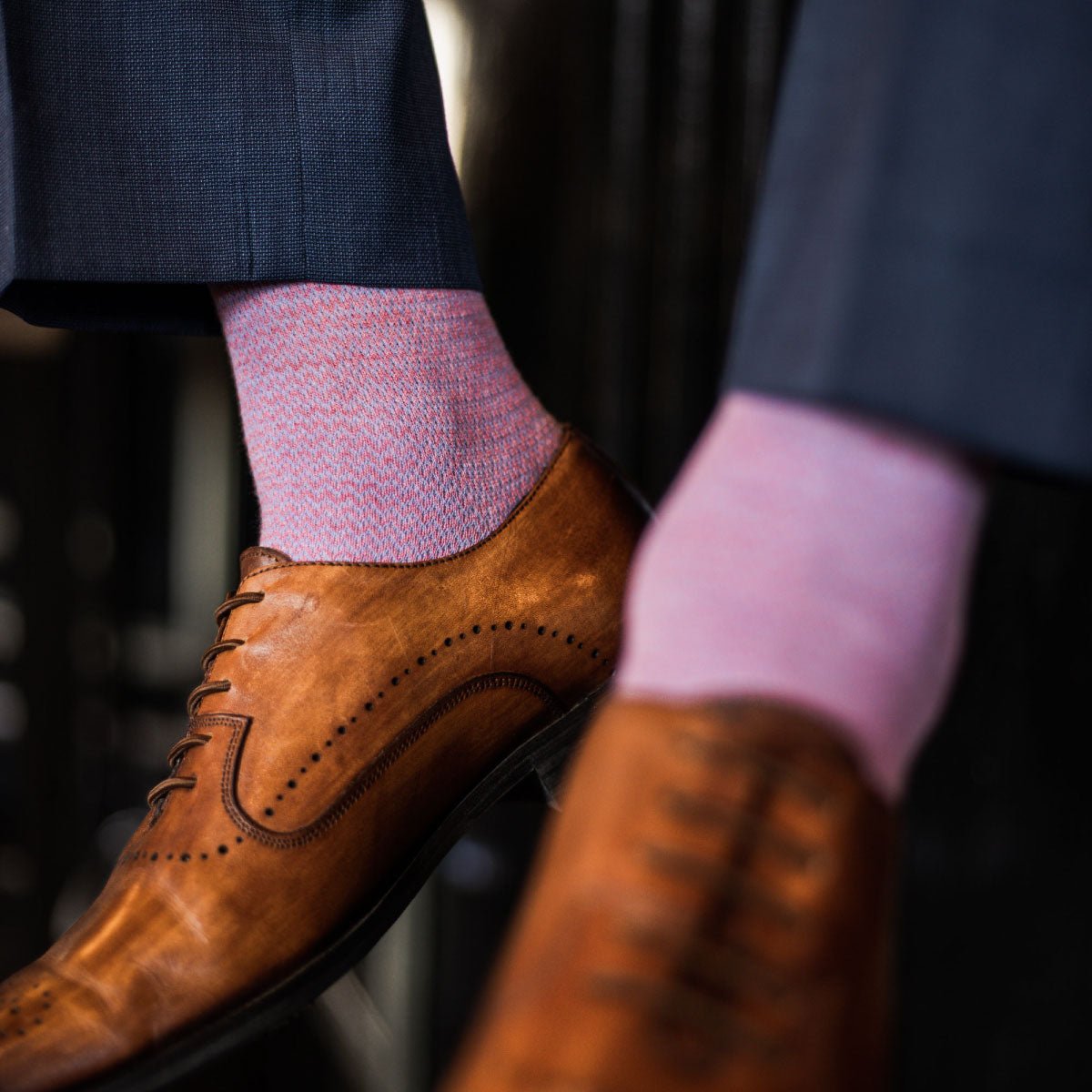 A man wearing blue trousers, pink and blue socks, and tan dress shoes.